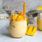 banana mango smoothie in a glass with a straw