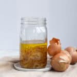 mason jar of onion oil with whole yellow onions next to it