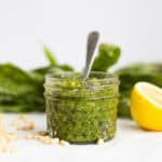 basil pesto in a small mason jar with basil leaves and lemon next to it