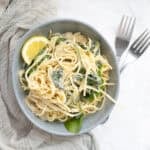 spinach artichoke spaghetti with a lemon in a bowl with forks next to it.