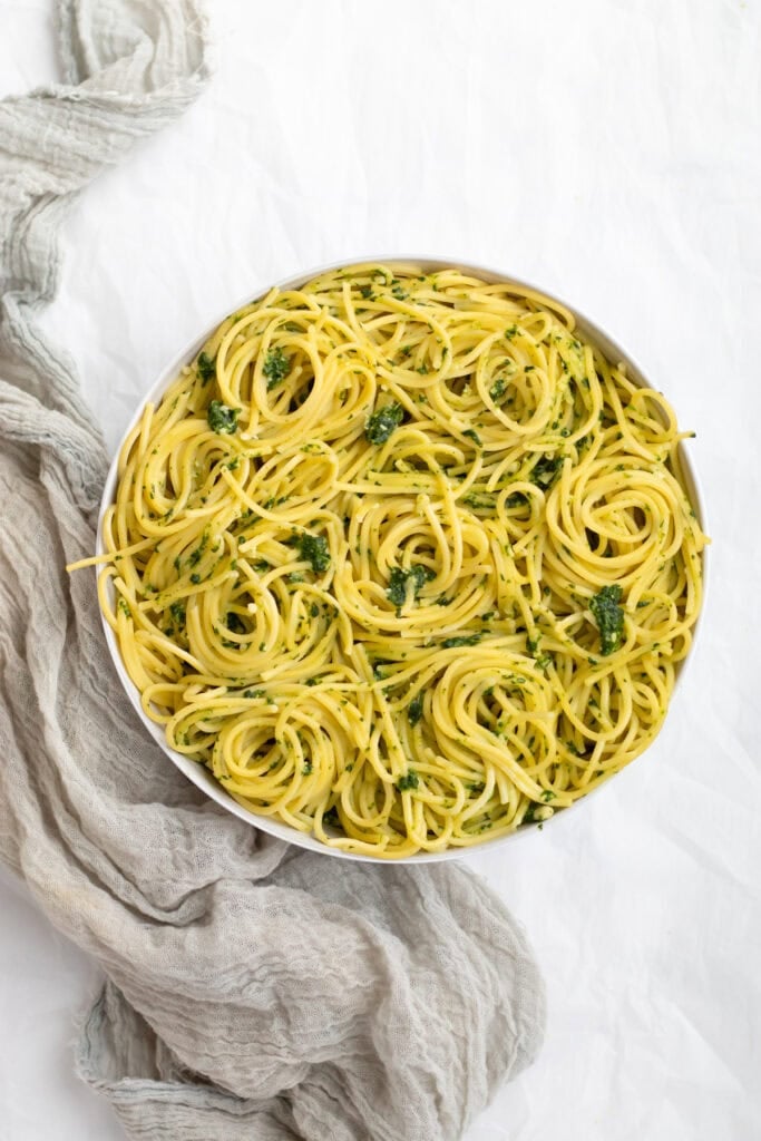 spinach pesto pasta swirled in a white serving bowl