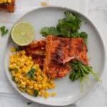 chili lime salmon on a white plate with corn and a lime