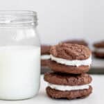 two chocolate sandwich cookies next to a glass of milk.