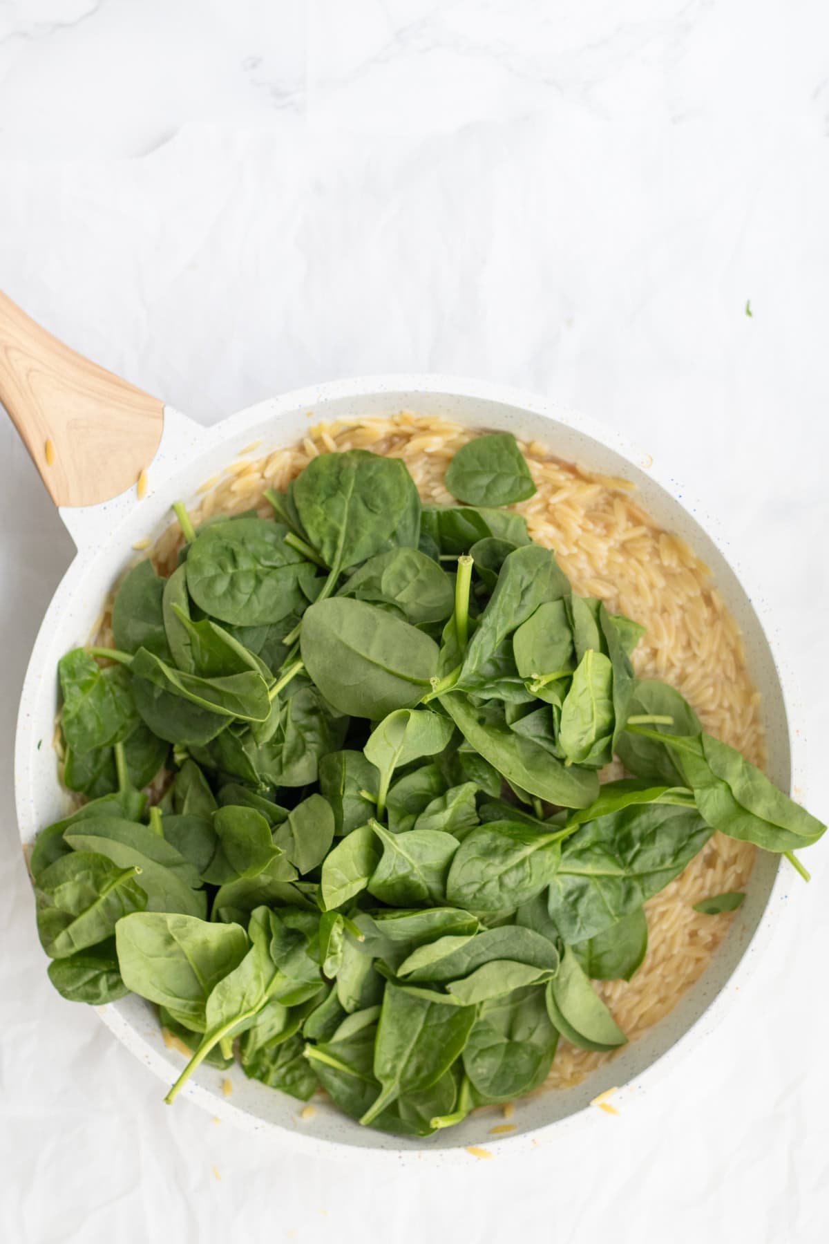 fresh spinach over cooking orzo in a frying pan