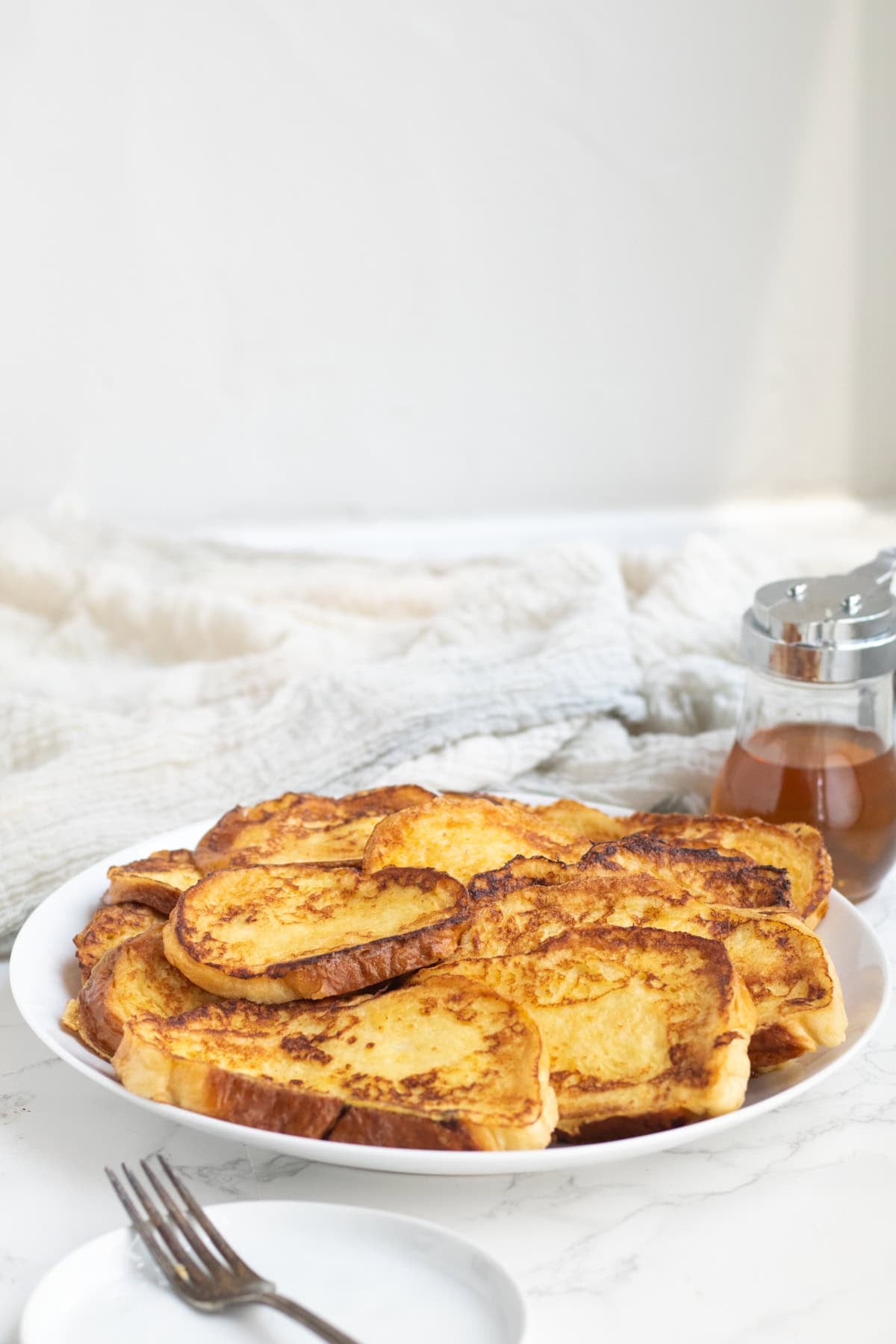 challah french toast on a white plate with syrup behind.