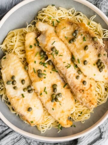fish in a serving bowl with a spoon over angel hair pasta