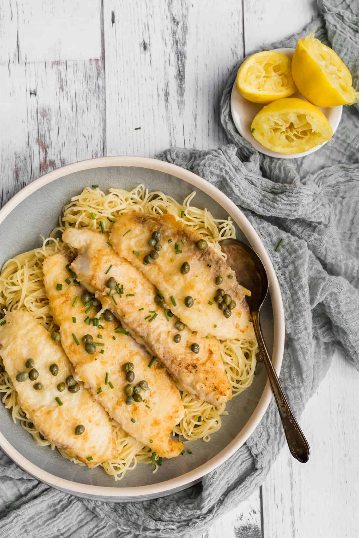fish piccata on a plate with a bowl of squeezed lemons