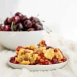 cherry dump cake on a white plate with a bowl of cherries behind
