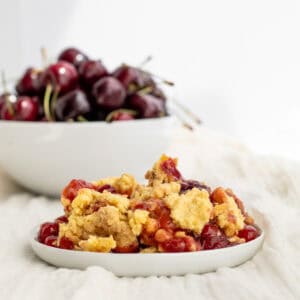 cherry dump cake on a white plate with a bowl of cherries behind