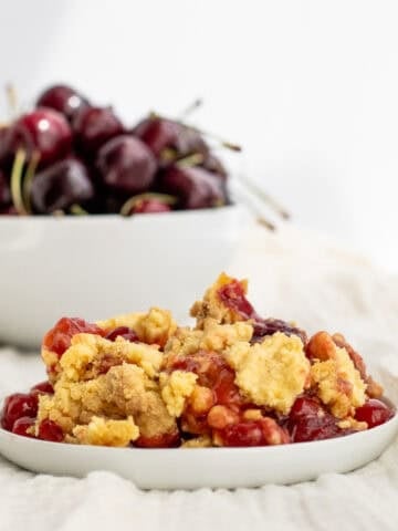 cherry dump cake on a white plate with a bowl of cherries behind