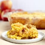 a scoop of apple dump cake on a white plate with rest of cake behind it
