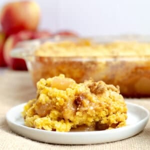 a scoop of apple dump cake on a white plate with rest of cake behind it