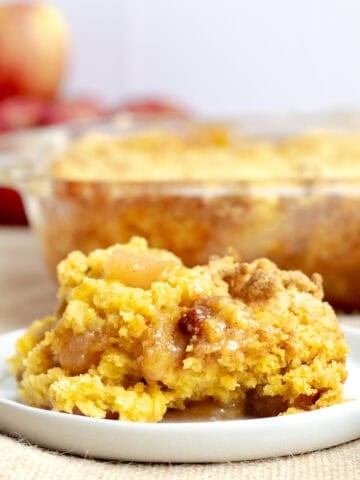 a scoop of apple dump cake on a white plate with rest of cake behind it