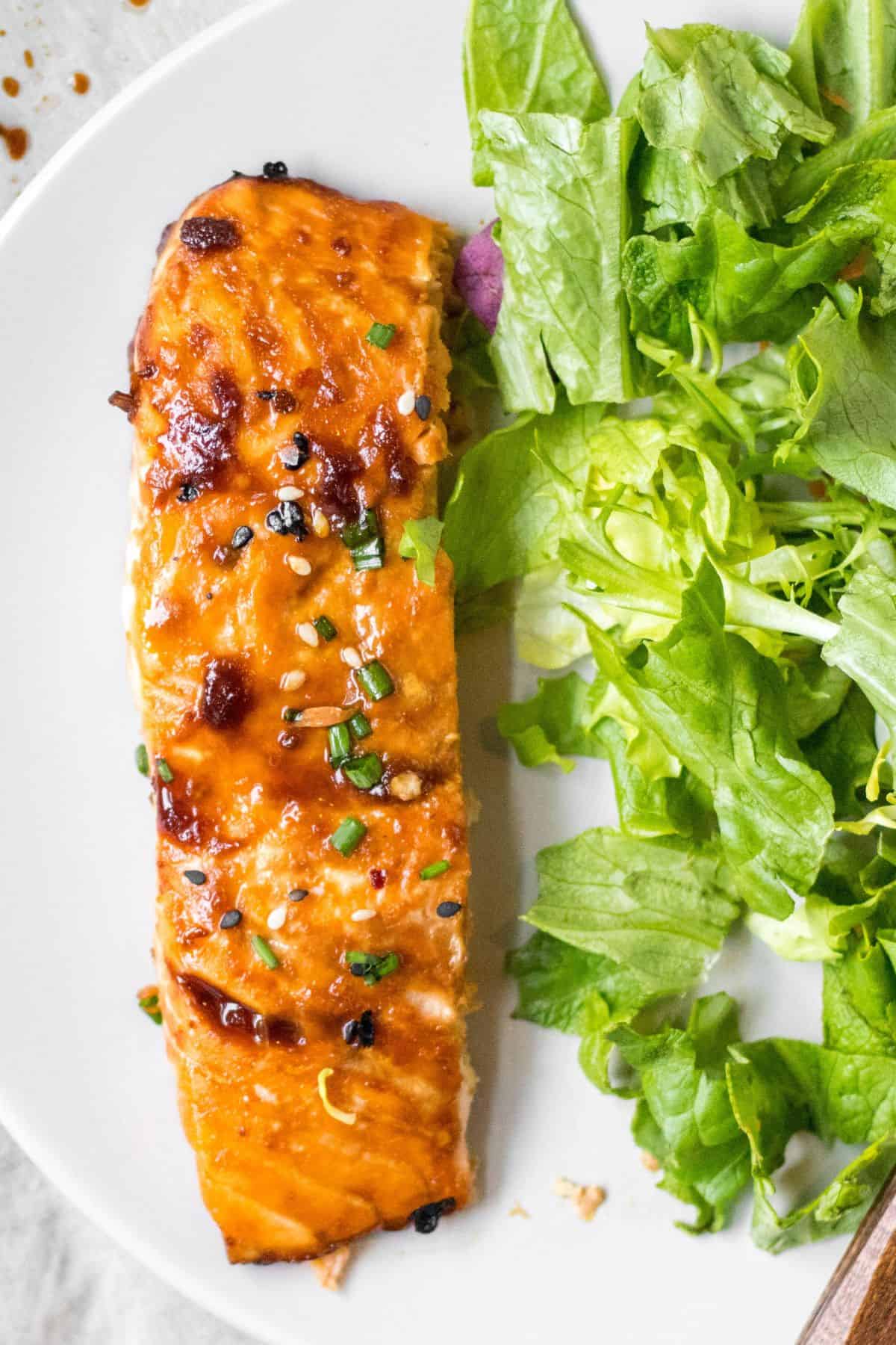 sesame ginger salmon on a white plate with a simple green salad.
