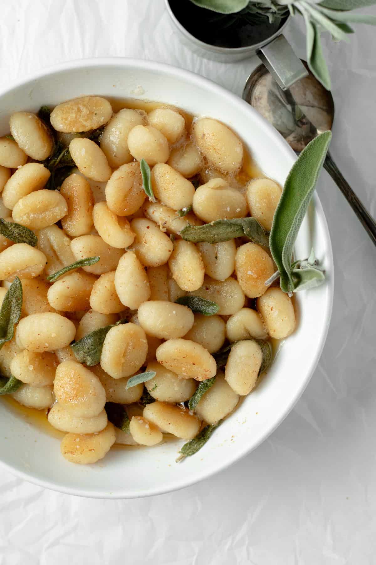 brown butter gnocchi in a white serving bowl with some sage leaves.