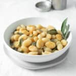 brown butter sage gnocchi in a white bowl with a vase of sage behind.