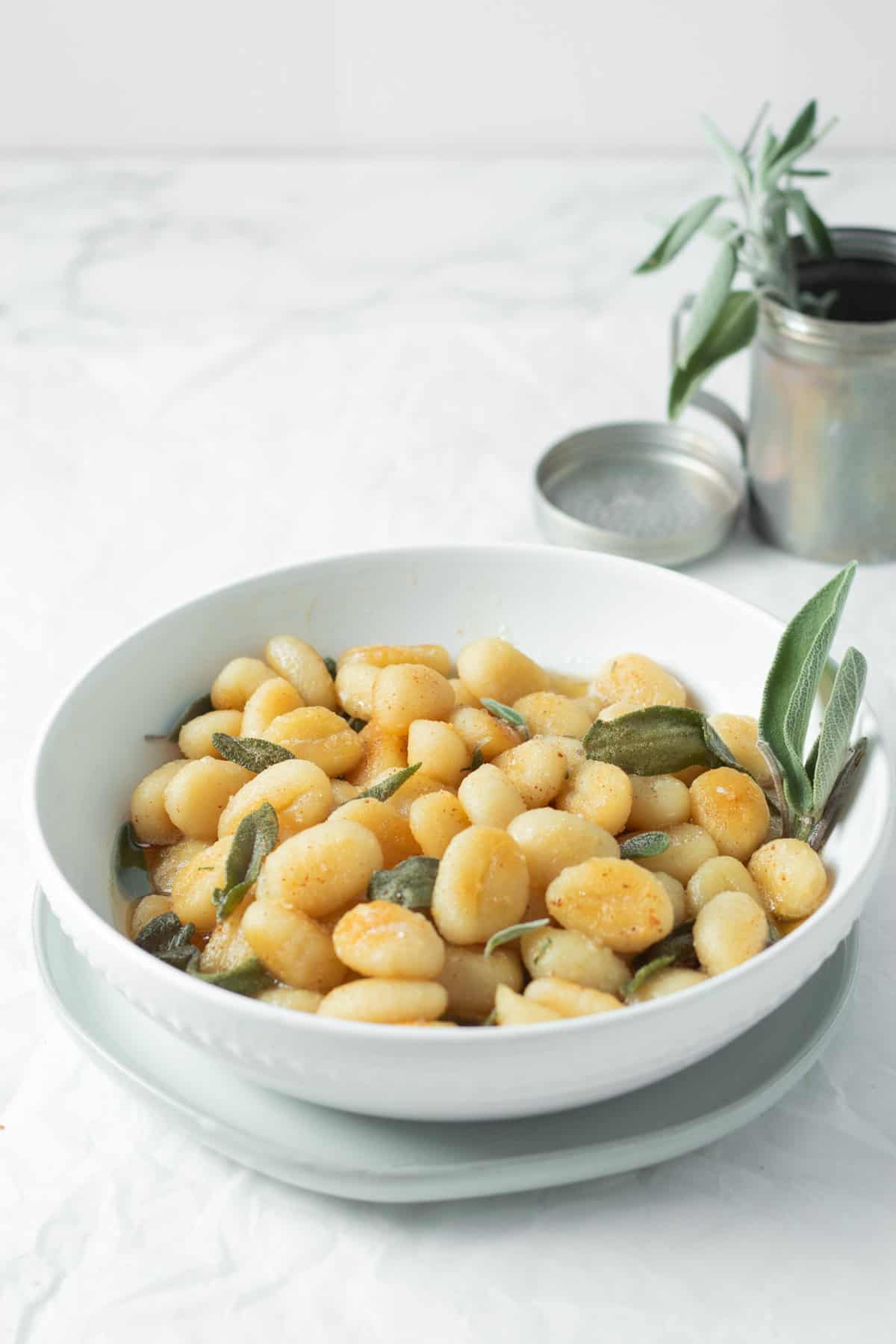 brown butter sage gnocchi in a white bowl with a vase of sage behind.