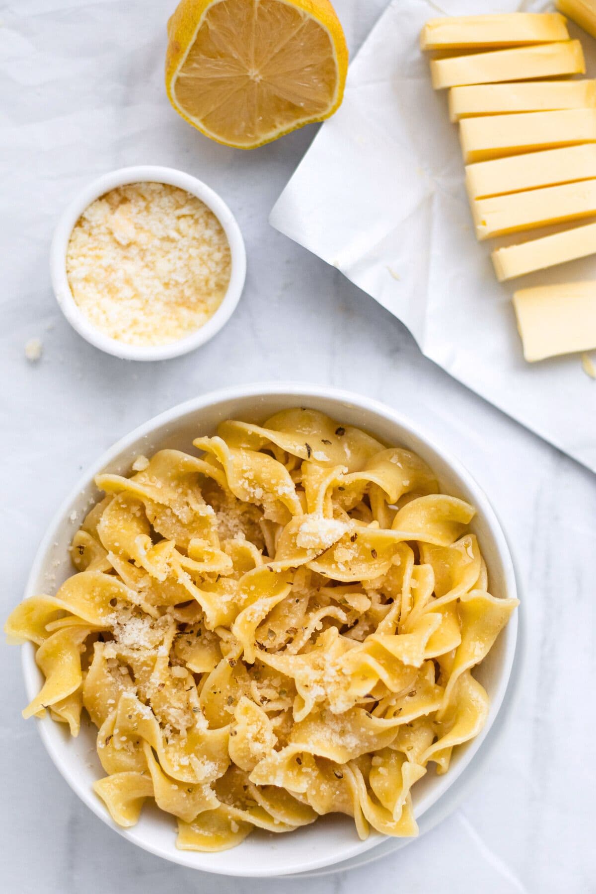 butter noodles in a bowl with butter, parm and lemon around it.