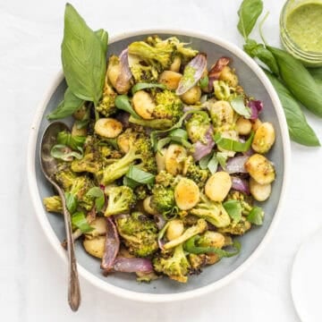 Sheet pan pesto gnocchi in a serving dish with a basil garnish.