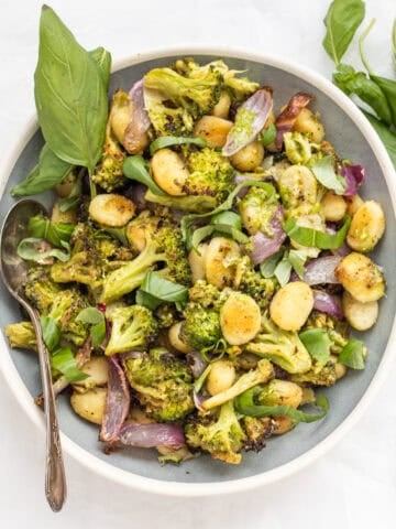 Sheet pan pesto gnocchi in a serving dish with a basil garnish.