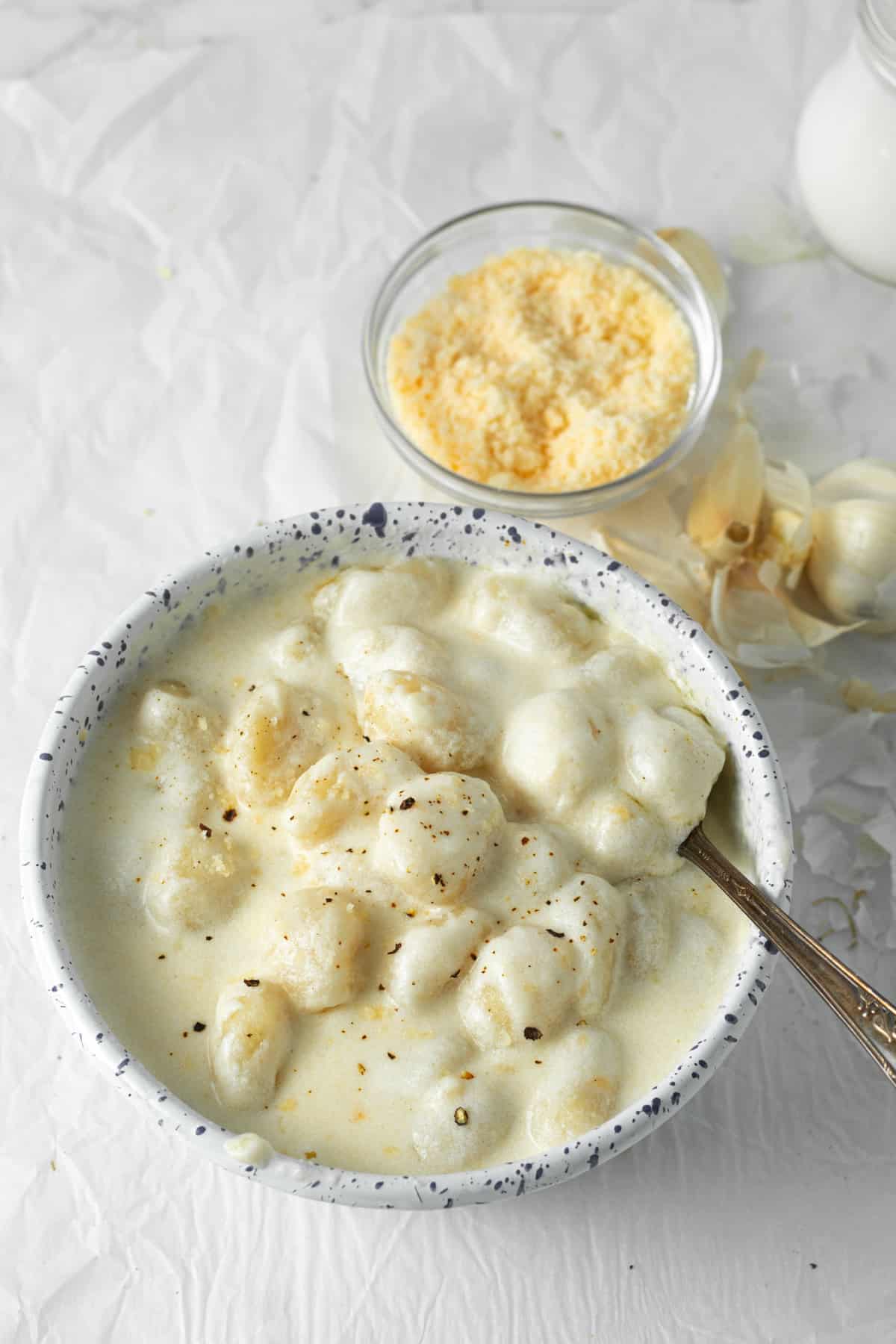 gnocchi alfredo in a serving bowl with a spoon and grated parmesan cheese in background. 