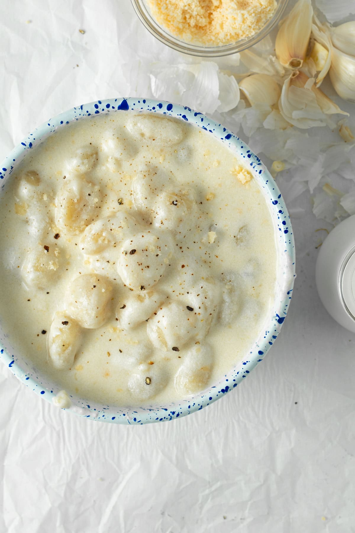 gnocchi alfredo in a serving bowl with a spoon and grated parmesan cheese in background.