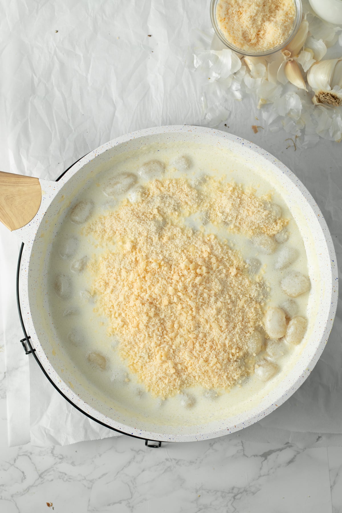 Grated Parmesan being stirred into gnocchi alfredo.