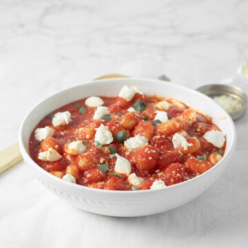 A white bowl full of gnocchi with mozzarella balls.