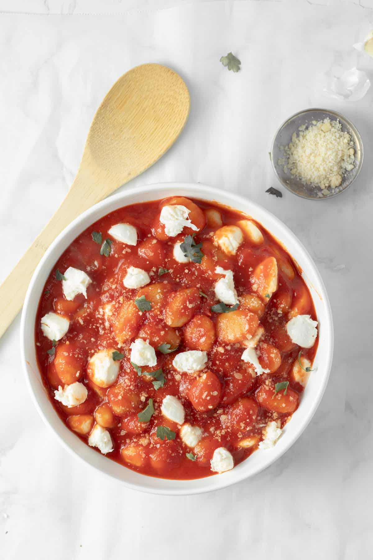 Gnocchi marinara with mozzarella balls and garnish in a white serving bowl.