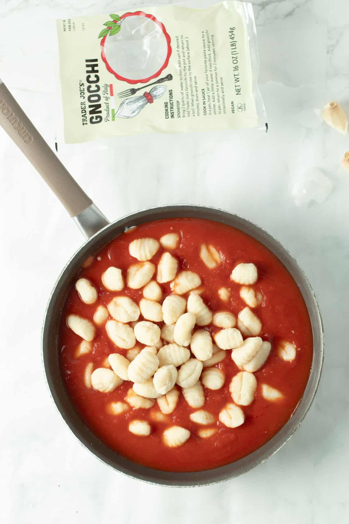 Raw gnocchi in a saute pan with marinara sauce.
