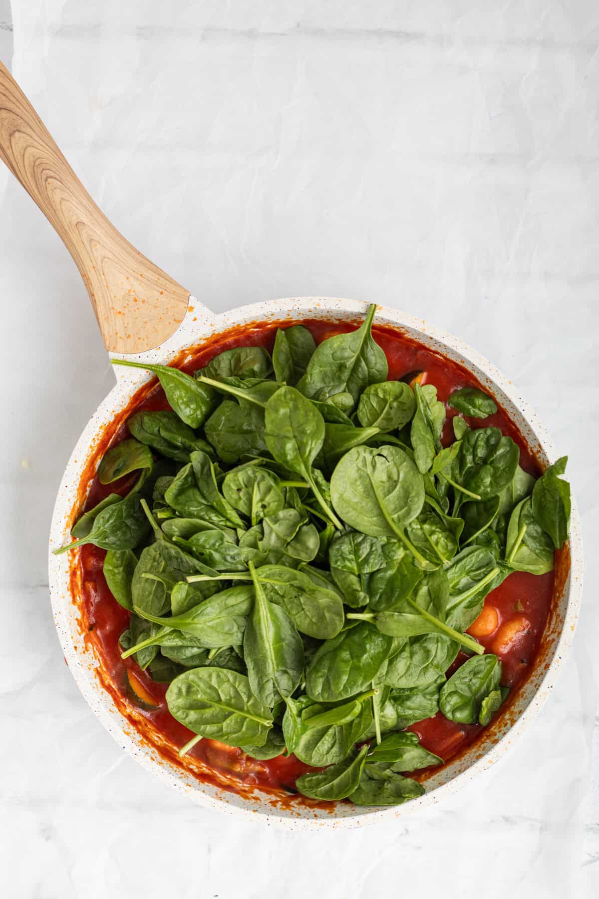 spinach being added a cooked gnocchi with vegetables.