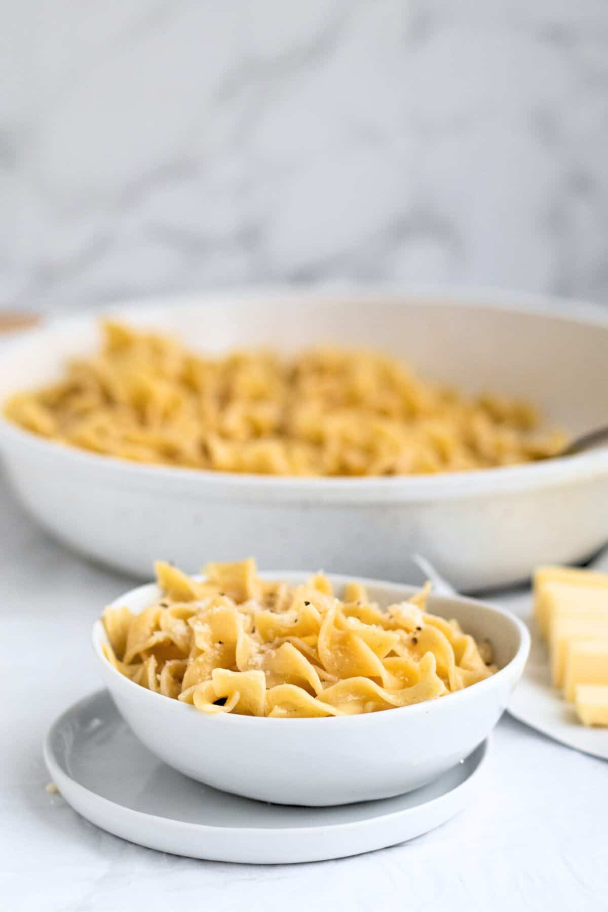 butter noodles in a white bowl with pan behind it.