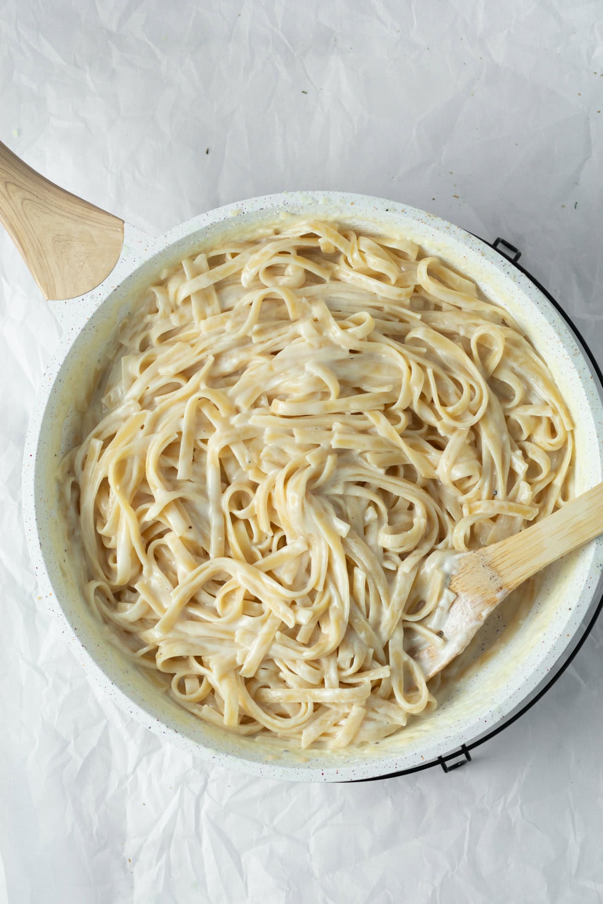 Wooden spoon stirring cooked fettuccine alfredo in a pan.