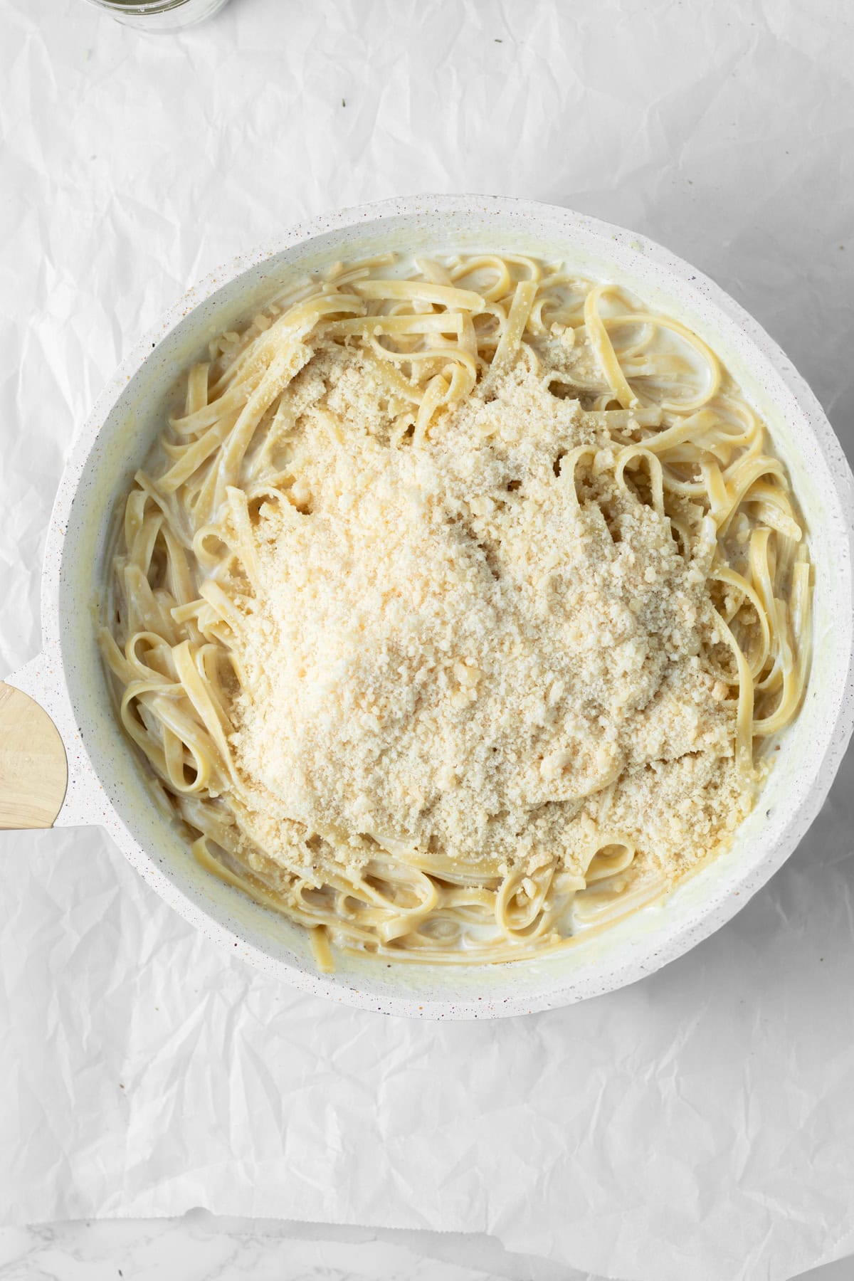 Parmesan cheese being added to pasta in a saute pan.