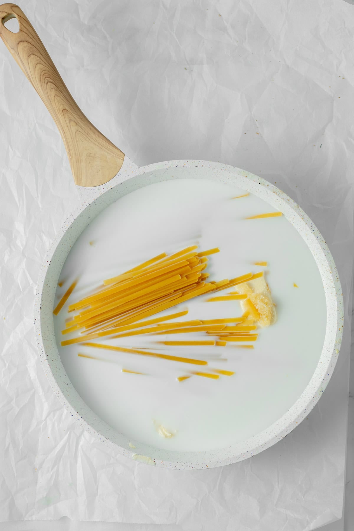 fettuccine noodles in in milk with butter and garlic in a saute pan.