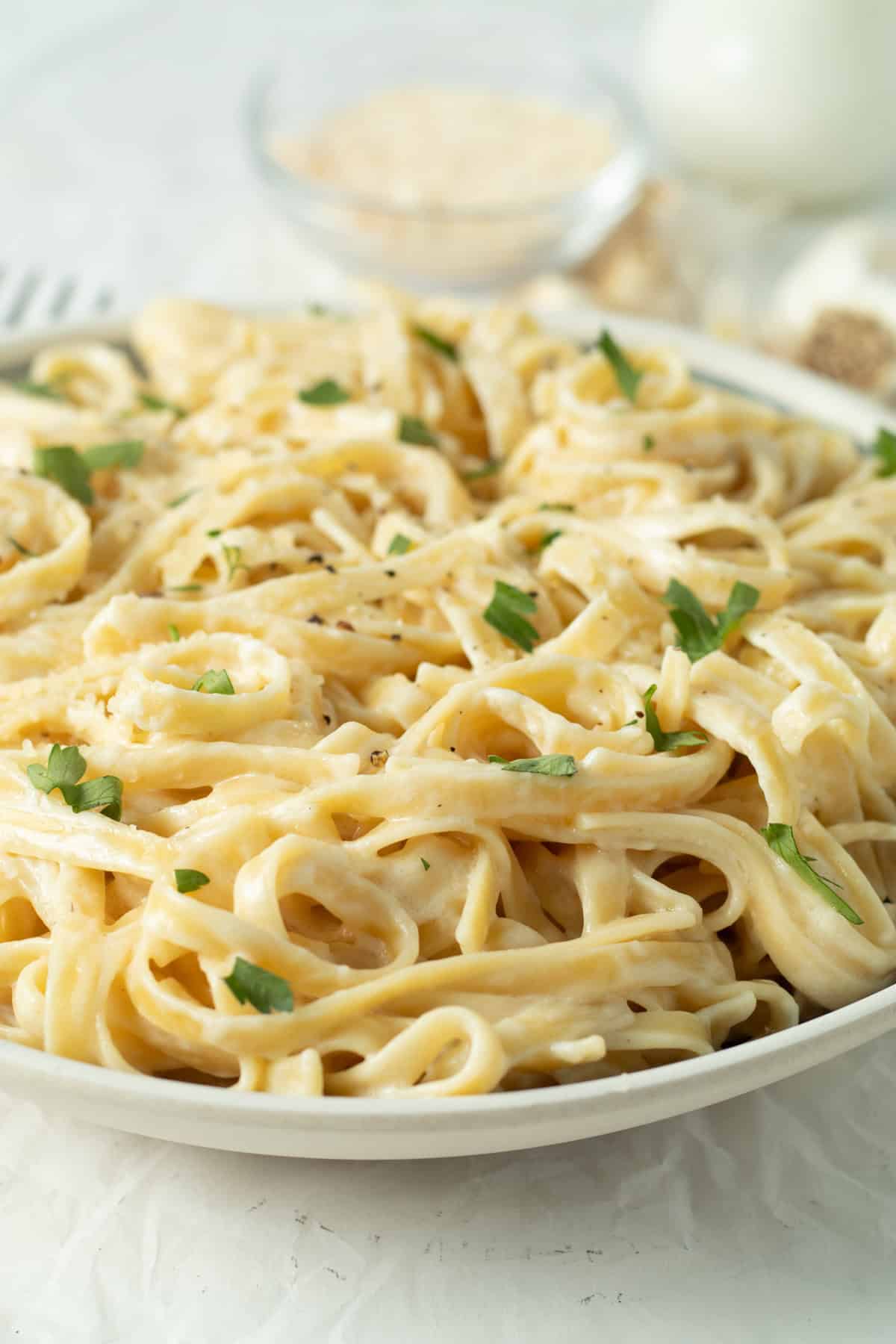 fettuccine alfredo in a white serving bowl with Parmasean cheese in the background.