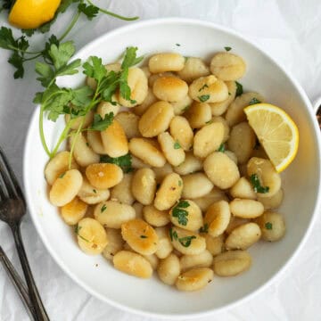 Crispy gnocchi in a white bowl garnished with lemon and parsley.