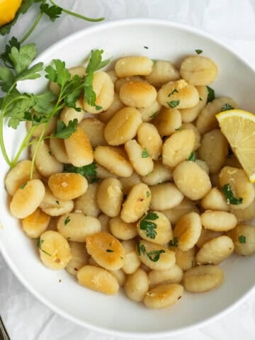 Crispy gnocchi in a white bowl garnished with lemon and parsley.