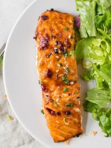 sesame ginger salmon on a white plate with a simple green salad.