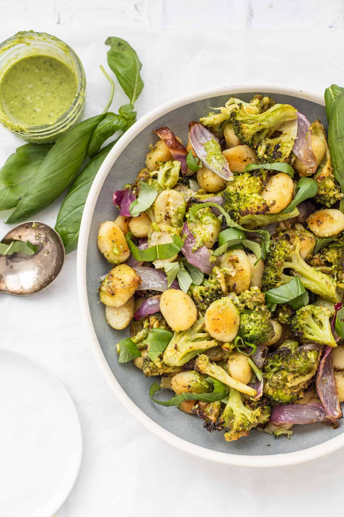 Sheet pan gnocchi with pesto in a serving dish with a basil and pesto on the side