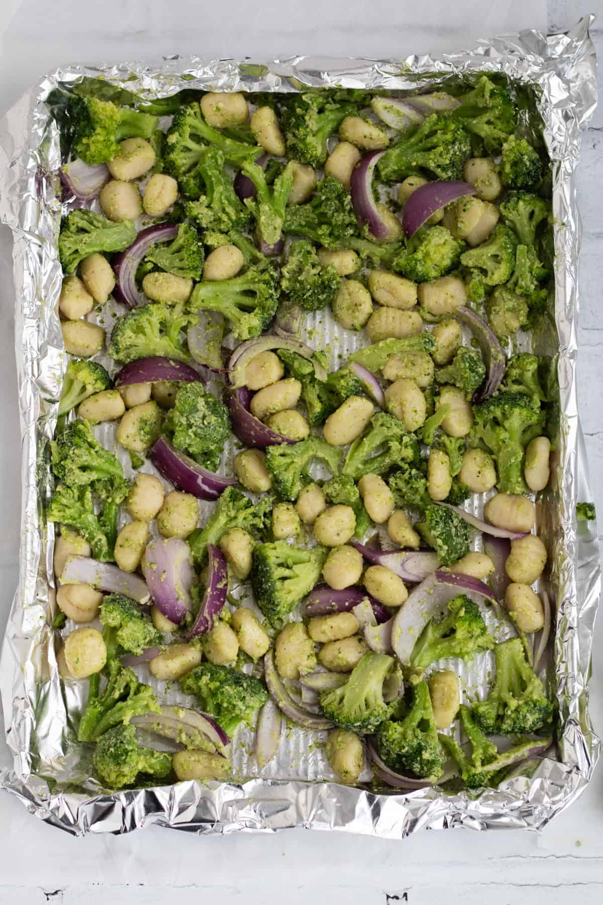 gnocchi, vegetables and pesto spread out on a sheet pan.
