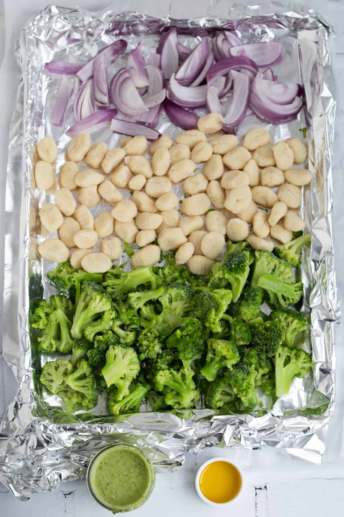red onion, gnocchi, broccoli, pesto and oil on a sheet pan.