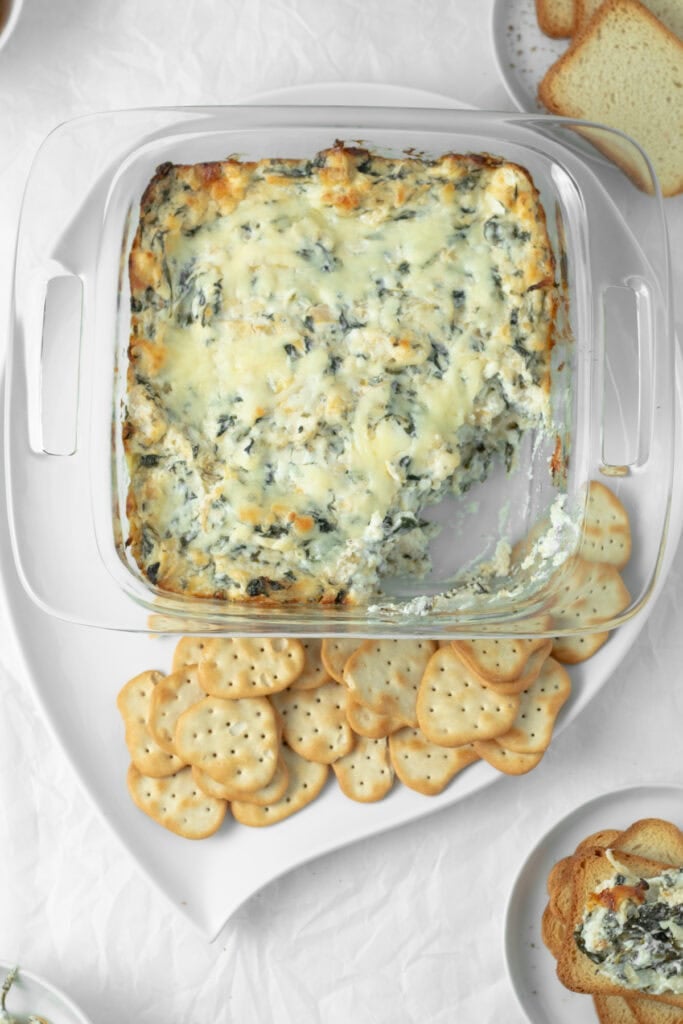 spinach artichoke dip with crackers on a serving plate.
