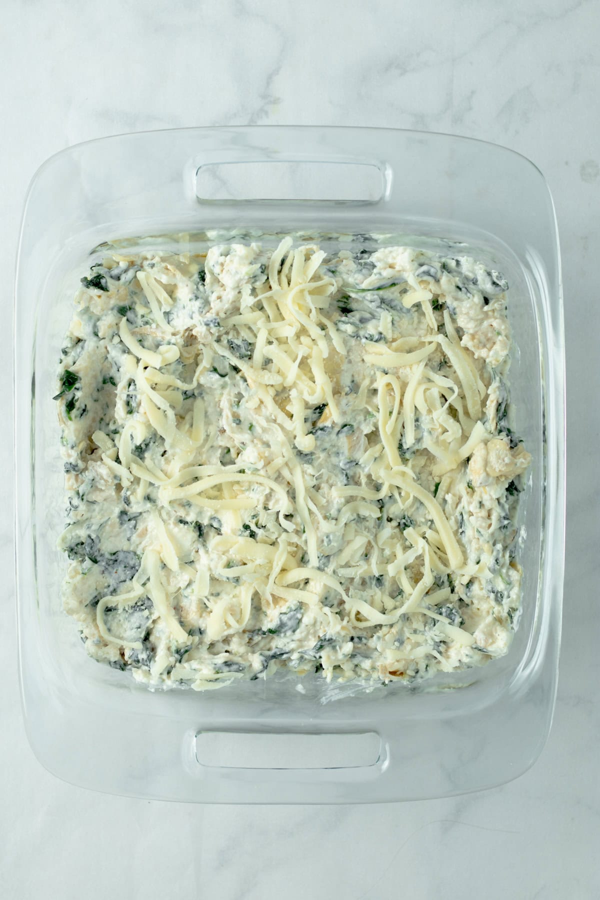 raw spinach artichoke dip topped with mozzarella in a glass baking dish.