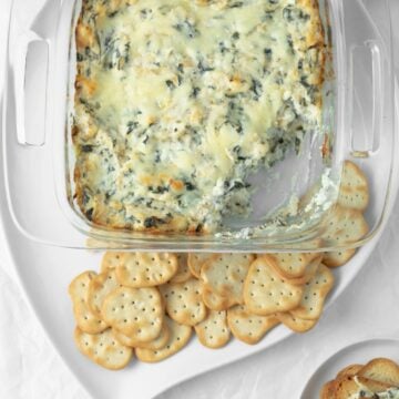 Baked spinach artichoke dip with a scoop taken out of it with crackers on a serving dish.
