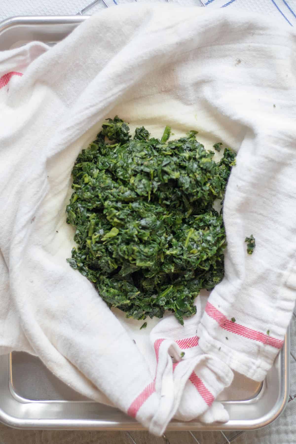 squeezing spinach out in a kitchen towel.