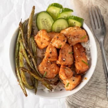 salmon bites in a rice bowl with cucumber and green beans.