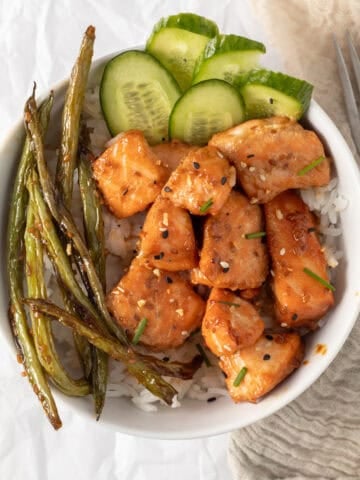 salmon bites in a rice bowl with cucumber and green beans.