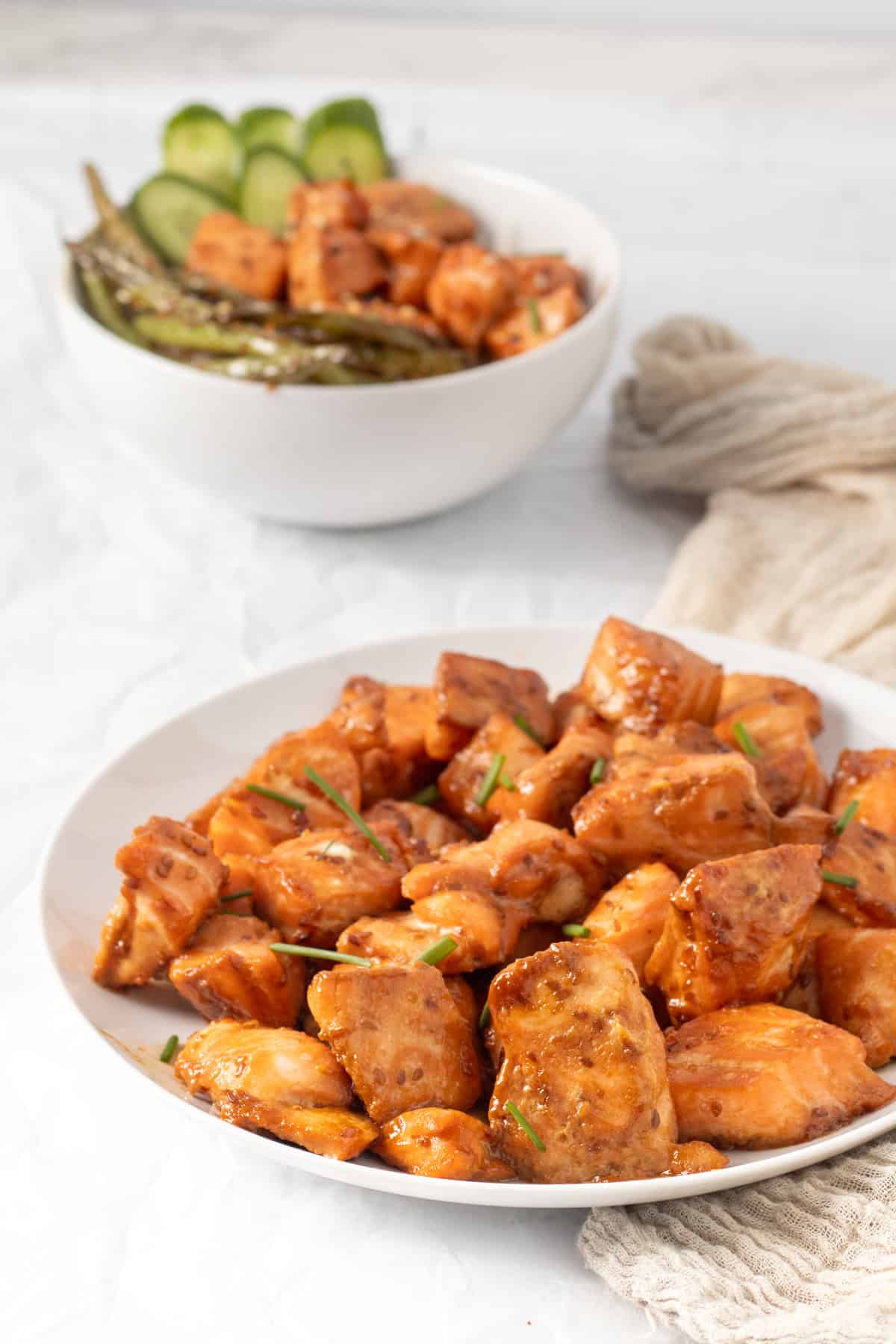 salmon bites on a white plate with a rice bowl in the background.