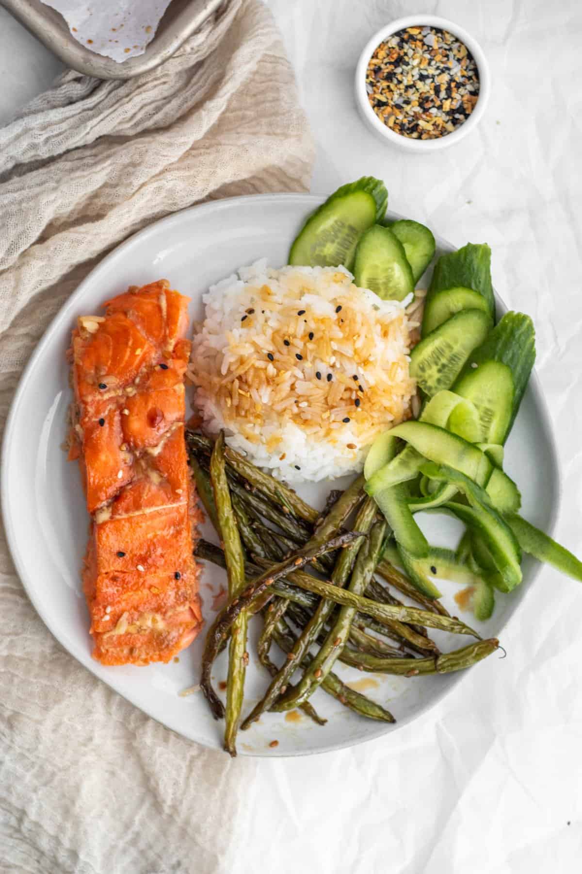 A plate with salmon, rice, cucumbers and green beans.